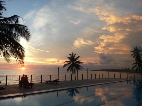 a man sitting on a bench next to a swimming pool at New Ocean Hill Hotel in Hikkaduwa
