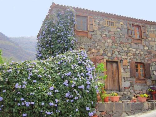 a stone house with purple flowers in front of it at La Finca' Landhaus in El Pie de la Cuesta