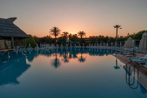 a swimming pool with chairs and a sunset in the background at AQI Pegasos World in Side