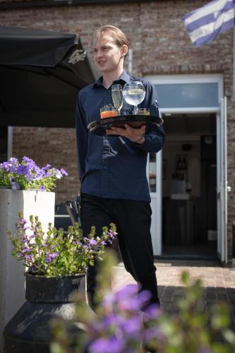 a man holding a tray with wine glasses on it at Hotel Groede in Groede