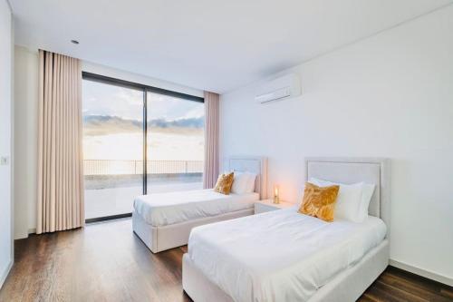 two beds in a room with a large window at Vila Cales e Chadas by Your Madeira Rentals in Arco da Calheta