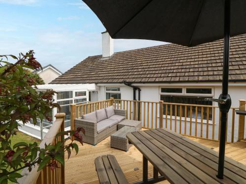 a wooden deck with a bench and an umbrella at Haul a Gwynt in Benllech