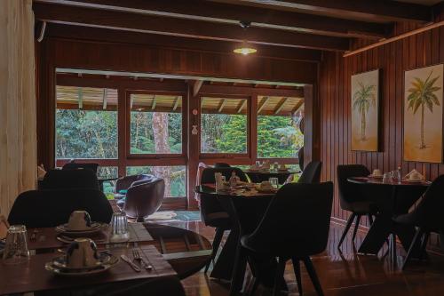 a dining room with tables and chairs and windows at Pousada Cantos e Contos in Monte Verde