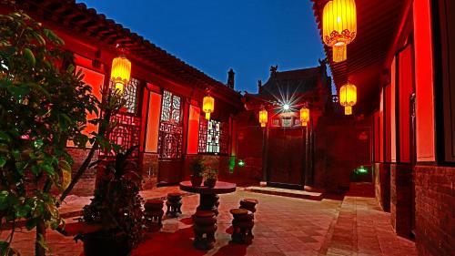 a courtyard with red buildings with a table and lights at Pingyao Xiangshengyuan Guest House in Pingyao