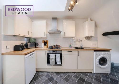 a kitchen with white cabinets and a washer and dryer at Comfortable and Homely 1-Bedroom 1-Bathroom Serviced Apartment, Free Parking, Free WiFi By Redwood Stays in Farnborough