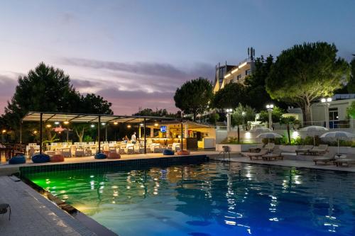 a swimming pool with chairs and a building at night at Edva Resort in Vlorë