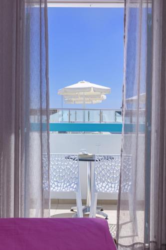 a table and a chair on a balcony with an umbrella at Santellini Hotel in Kamari
