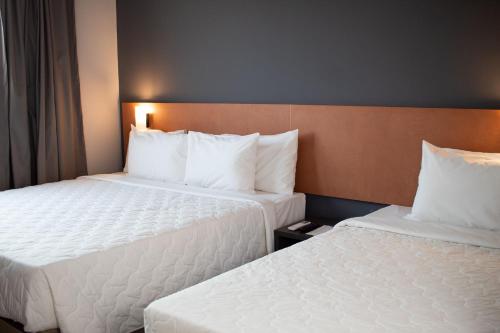 two beds in a hotel room with white pillows at Comfort Hotel Presidente Prudente in Presidente Prudente