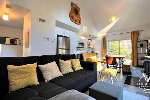 a living room with a black couch and a kitchen at Le2089 - Spa et plage - Les chalets dans le nord in Sainte-Lucie-de-Doncaster