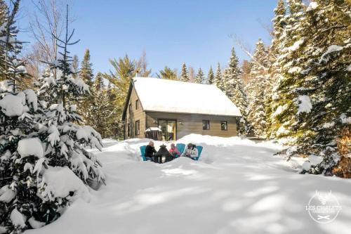 two people sitting in the snow in front of a cabin at Le2089 - Spa et plage - Les chalets dans le nord in Sainte-Lucie-de-Doncaster