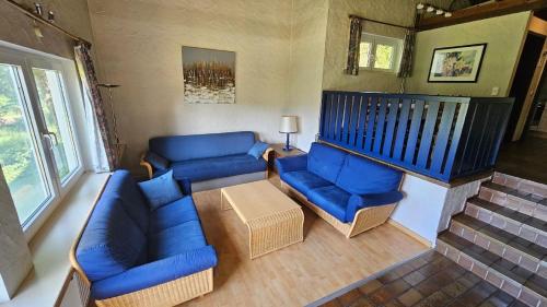 un salon avec des canapés bleus et une table dans l'établissement Ferienhaus mit Garten im Naturpark Südeifel, à Biersdorf am See