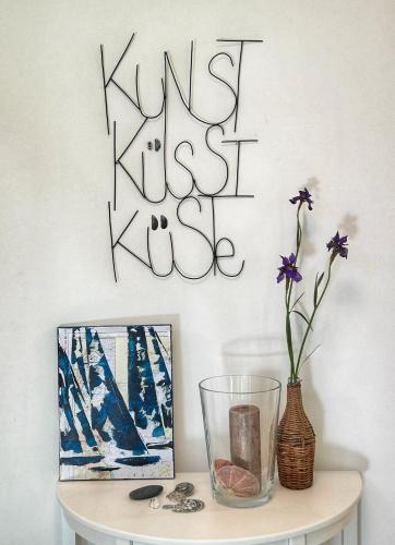 a sign on a wall with a vase on a table at Kunst küsst Küste in Hohwacht
