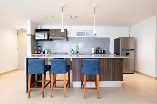 a kitchen with a counter with four blue bar stools at Ocean Breeze, Cancun Sanctuary - HiveNB in Cancún