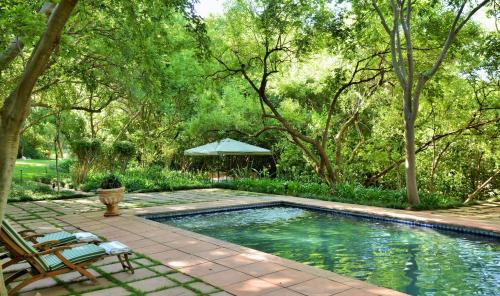 a swimming pool in a garden with chairs and a tent at De Hoek Country Hotel in Magaliesburg