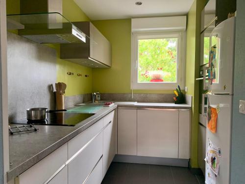 d'une cuisine avec des murs verts, des armoires blanches et une fenêtre. dans l'établissement Maison au calme dans le golf de Lacanau, à Lacanau