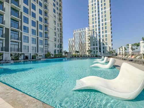 a large swimming pool with two white sculptures in a city at Vacationer Holiday Homes I Modern 1 Bedroom I Peaceful Location I Near Dubai Hills Mall & Park in Dubai