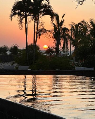 a pool with palm trees and the sunset in the background at Villa Praia - La Villa Group in Jericoacoara