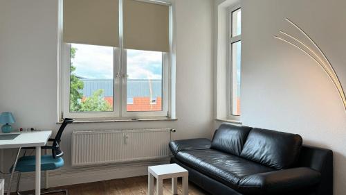 a living room with a black leather couch and two windows at Zentrale Monteurwohnung Neumünster mit Küche & WLAN in Neumünster