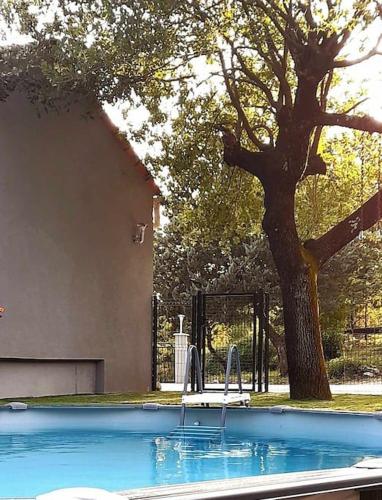 une piscine avec un arbre en face d'un bâtiment dans l'établissement Gîte VILLA ROMAN Vogüé, à Vogüé
