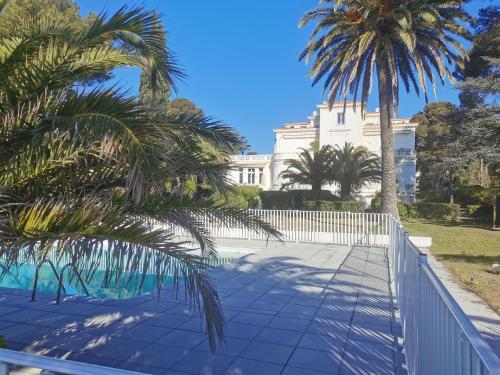 une clôture devant un bâtiment blanc avec des palmiers dans l'établissement Rivages Palladio, à Saint-Raphaël