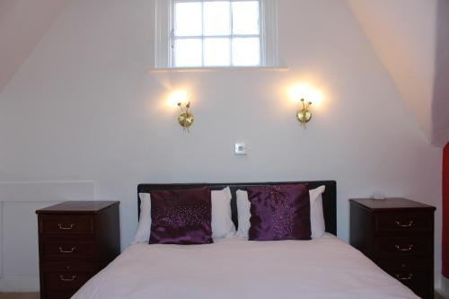 a bedroom with a bed with purple pillows and a window at The George Hotel Stansted Airport in Bishops Stortford