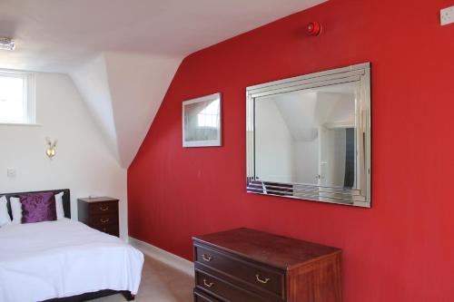a red bedroom with a bed and a mirror at The George Hotel Stansted Airport in Bishops Stortford