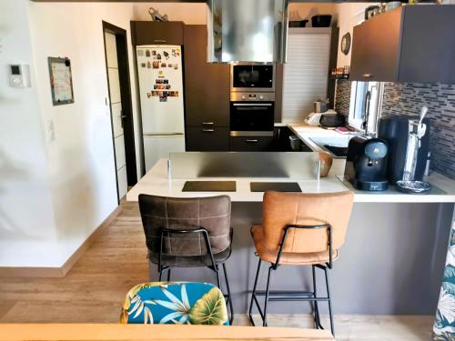 une cuisine avec un comptoir et deux tabourets de bar dans l'établissement L Oiseau du Paradis, à Les Sables-dʼOlonne