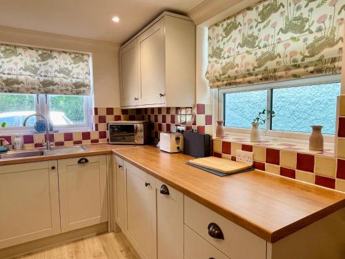 a kitchen with a counter with a microwave and two windows at 3-bed cottage in Sway, New Forest (5 min walk from Sway Train Station) in Sway