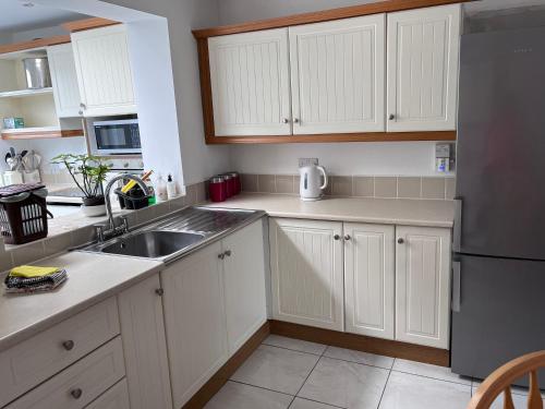 a kitchen with white cabinets and a sink and a refrigerator at Spacious 5 double bed bedroom bungalow near Belfast in Lisburn