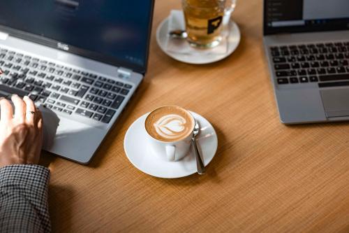 a person sitting at a table with a cup of coffee and a laptop at ATLANTIC Hotel Münster in Münster