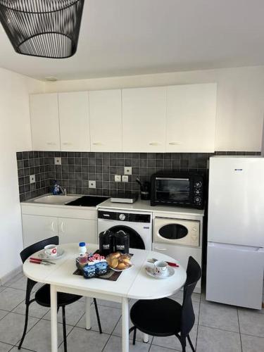 Il comprend une cuisine équipée d'une table blanche avec des chaises et d'un réfrigérateur blanc. dans l'établissement Hébergement Studio, à Saint-Martin-des-Noyers