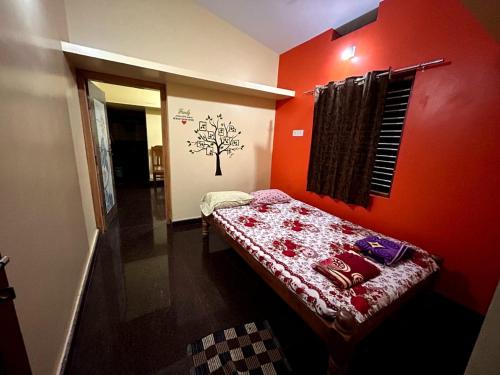 a room with a red wall with a bed in it at Shreeniketana stay in Mādangeri