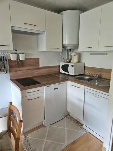 une cuisine avec des armoires blanches, un évier et un micro-ondes dans l'établissement Appartement au coeur de Saint Lary Soulan, à Saint-Lary-Soulan