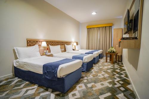 a hotel room with three beds and a flat screen tv at Osturat Emaar Hotel in Mecca