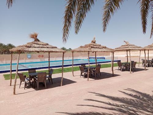 a group of tables and chairs with umbrellas next to a pool at Garden12 Outdoor & More in Douz