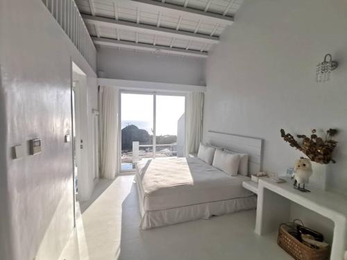 a white bedroom with a bed and a window at Ample Villa 小希臘民宿 in Ruifang