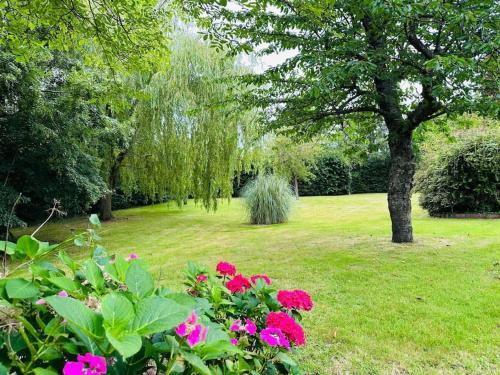un parc avec des fleurs roses et un arbre dans l'établissement Le Paradis du Breuil, à Le Breuil-en-Auge