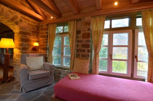a bedroom with a pink bed and a chair and windows at Papaevangelou Hotel in Papigko