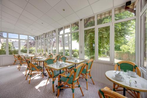 a row of tables and chairs in a room with windows at Brit Hotel Confort Bagnoles Normandie in Bagnoles de l'Orne