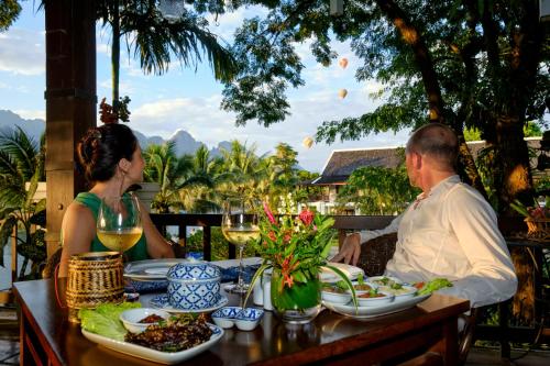 un uomo e una donna seduti a un tavolo con cibo e vino di Riverside Boutique Resort, Vang Vieng a Vang Vieng