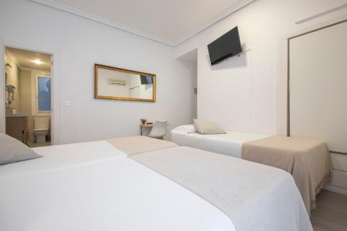 a white room with two beds and a television at Pensión Donostiarra in Donostia-San Sebastián