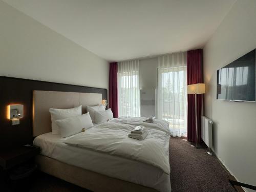 a bedroom with a large white bed with windows at Fontane Hotel in Schorfheide