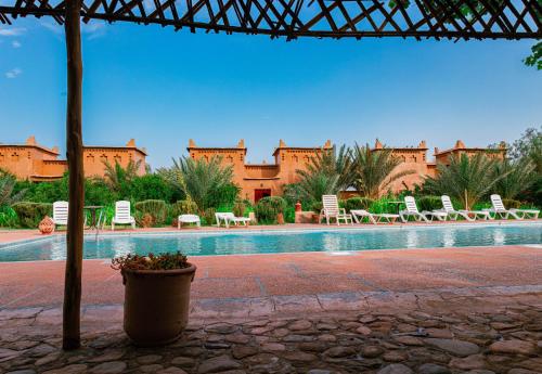 a resort with a swimming pool with chairs and a building at Maison D'h&ocirc;te Amridil in Skoura