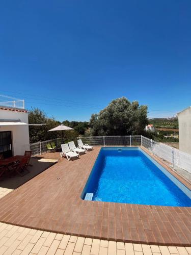 a swimming pool on a patio with chairs and a house at Casa Portela in Vila Nova De Cacela