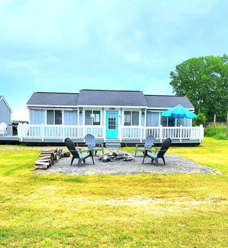 a house with chairs and a table in front of it at Cottage lake view with Deck and BBQ Grill in Three Mile Bay