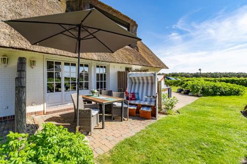 a patio with an umbrella and a table and chairs at Adis Meerblick Landhaus Arnika HT 2 in Wenningstedt