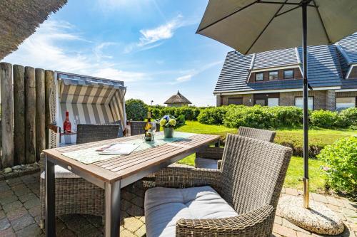 a patio with a wooden table and chairs and an umbrella at Adis Meerblick Landhaus Arnika HT 2 in Wenningstedt
