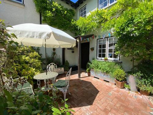 a patio with an umbrella and a table and chairs at Cedra Cottage - Vintage Country Hideaway in Axminster