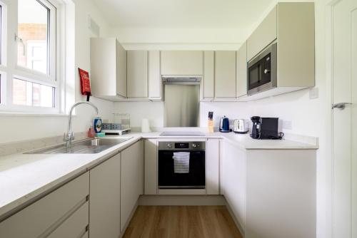 a white kitchen with white cabinets and a sink at PenthouseStays Wimbledon - Chic 2 Bedroom King Bed Apartment with Balcony - 2 mins from Wimbledon Tennis Club and Museum - AELTC in London