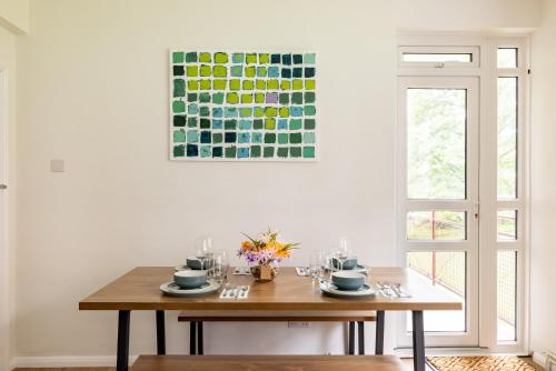 a table in a dining room with a painting on the wall at PenthouseStays Wimbledon - Chic 2 Bedroom King Bed Apartment with Balcony - 2 mins from Wimbledon Tennis Club and Museum - AELTC in London